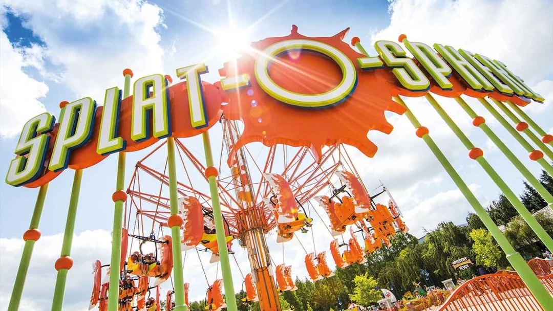 Splat-O-Sphere ride with orange swings and green poles under a sunny sky.