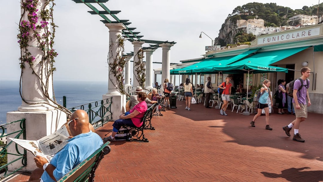 Capri promenade with people relaxing and walking near Funicolare, overlooking the sea.