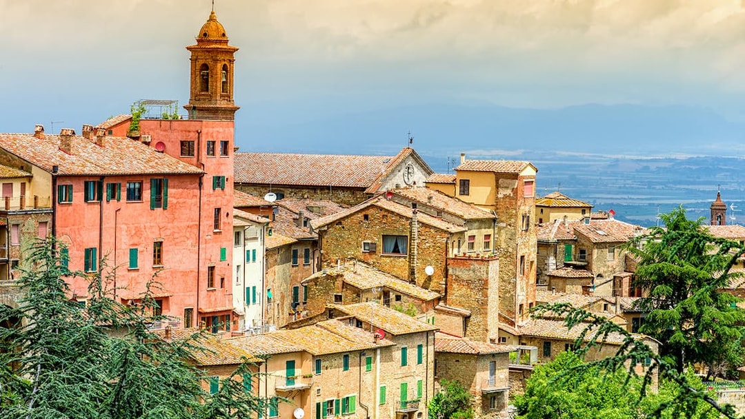 Val D’Orcia village with rustic buildings and a bell tower, Tuscany landscape in the background.