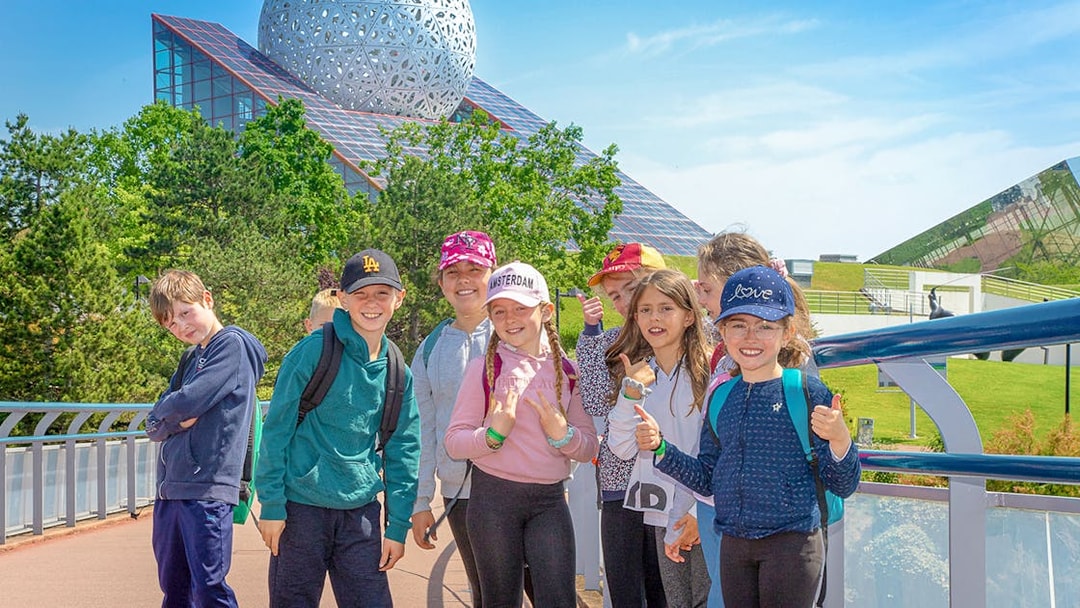 Group of children smiling in front of Futuroscope's architectural dome in France.