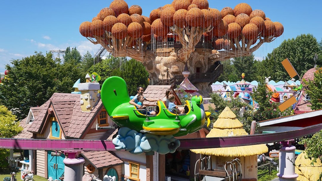 Visitors enjoying a ride at Gardaland Park with whimsical treehouse in background.