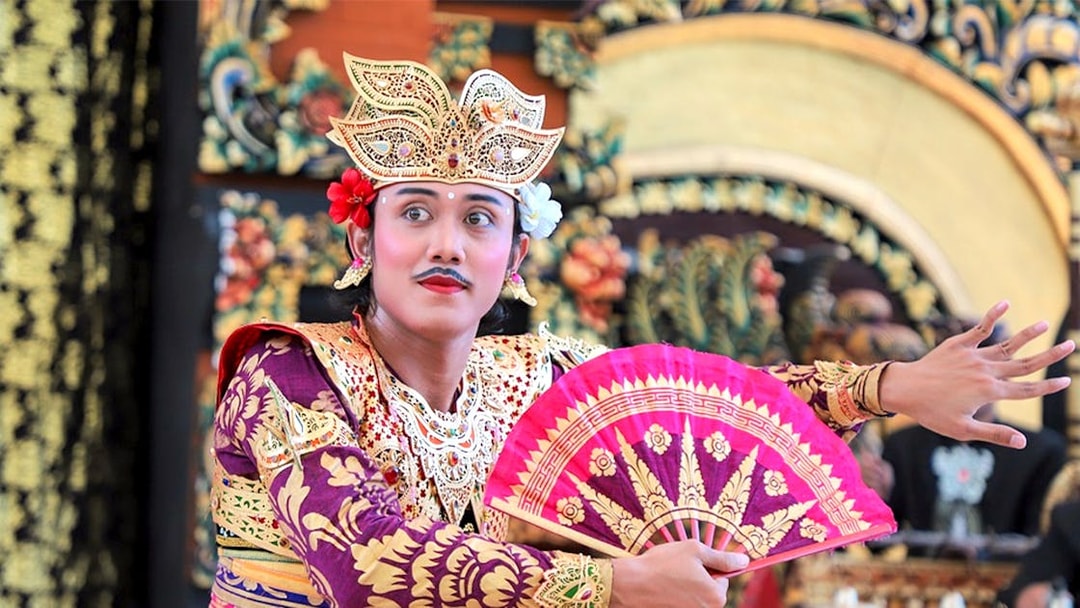 Balinese dancer performing at Garuda Wisnu Kencana at night, holding a decorative fan.