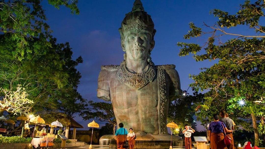 Garuda Wisnu Kencana statue at dusk in Bali's culture park, surrounded by visitors.