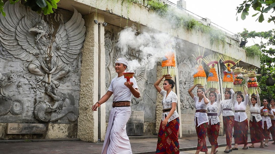 Balinese procession at Garuda Wisnu Kencana Culture Park, Bali, with traditional offerings.