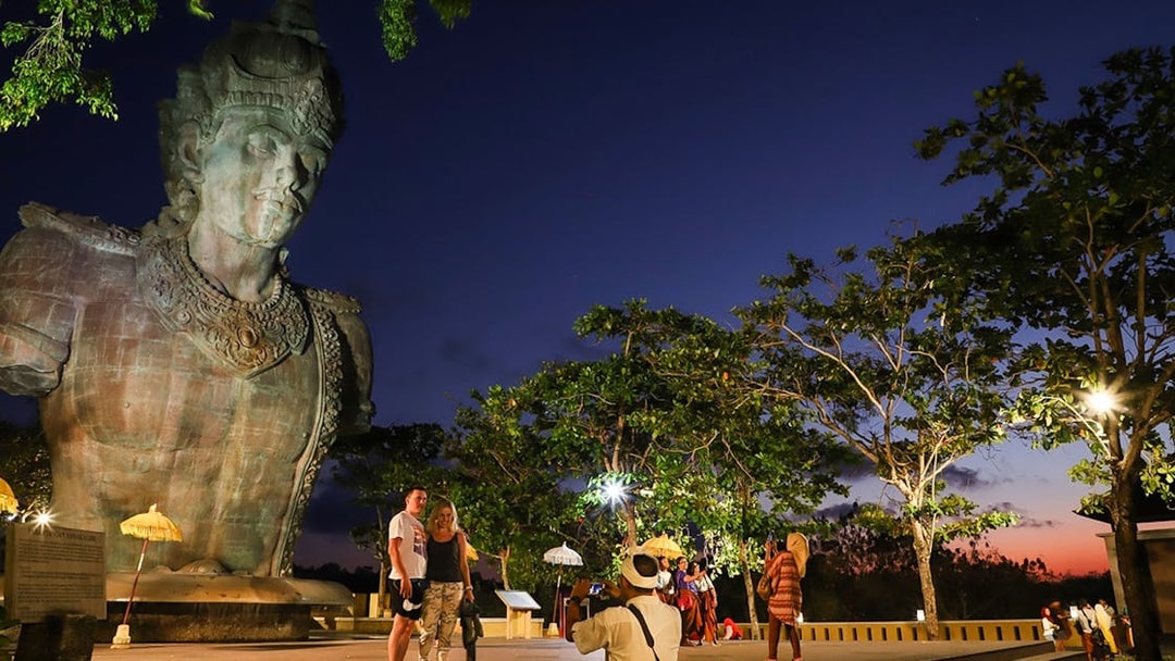 Visitors at Garuda Wisnu Kencana Culture Park in Bali at sunset, with the statue in view.