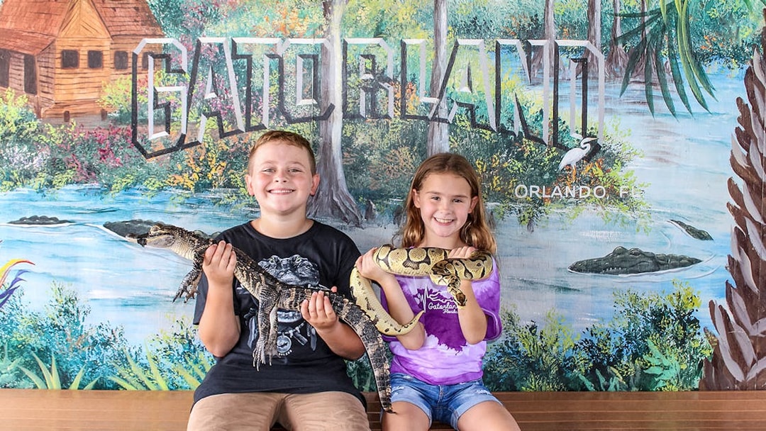 Children holding reptiles at Gatorland, Orlando backdrop.