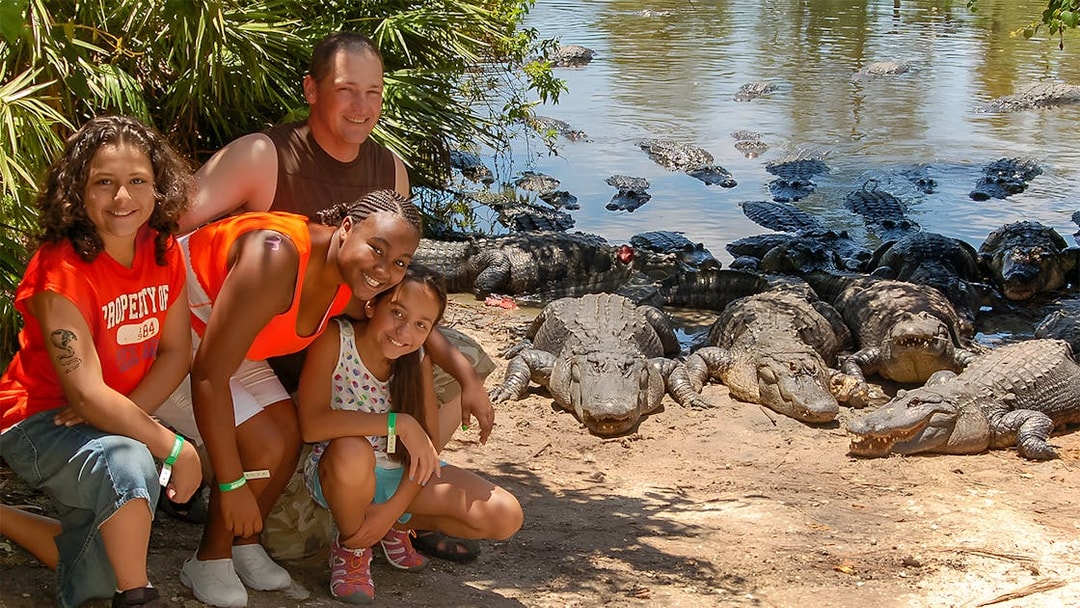 Group posing near alligators at Gatorland with Screamin’ Gator Zip Line in background.