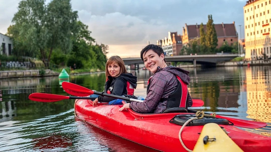 Kayakers paddling on a river in Gdansk with historic buildings in the background.