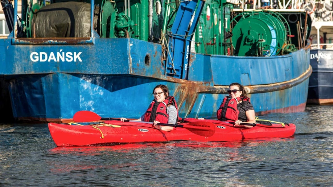 Two people kayaking near a ship in Gdańsk during a private tour.