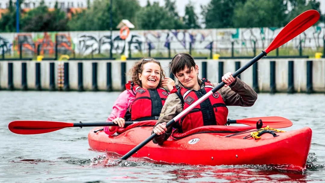 Two people kayaking on a private tour near a graffiti-covered wall.