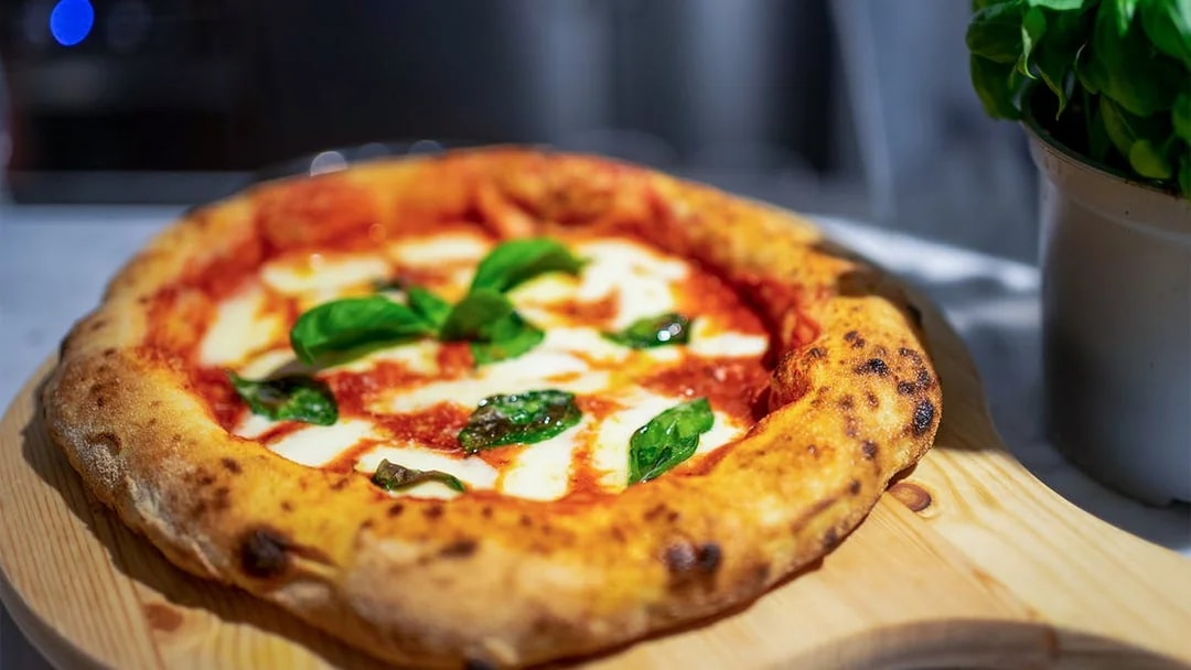 Pizza with fresh basil on a wooden board during a cooking class in Milan.