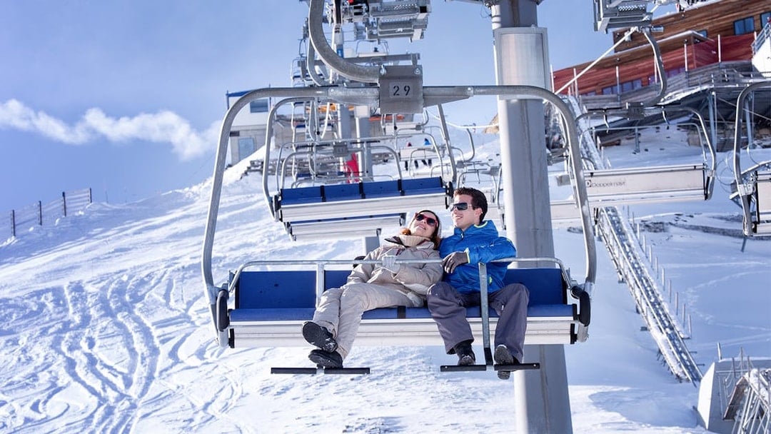 Couple on cable car at Glacier 3000 with snowy mountain backdrop.