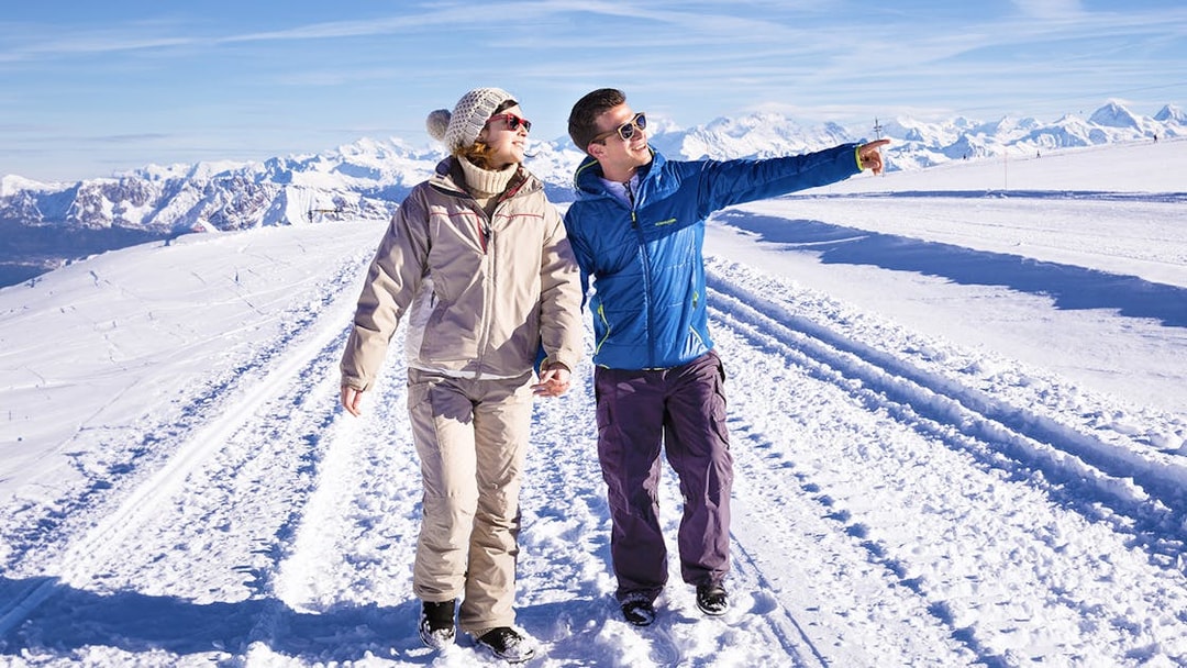 Couple walking on snowy path at Glacier 3000, Montreux, with scenic mountain views.
