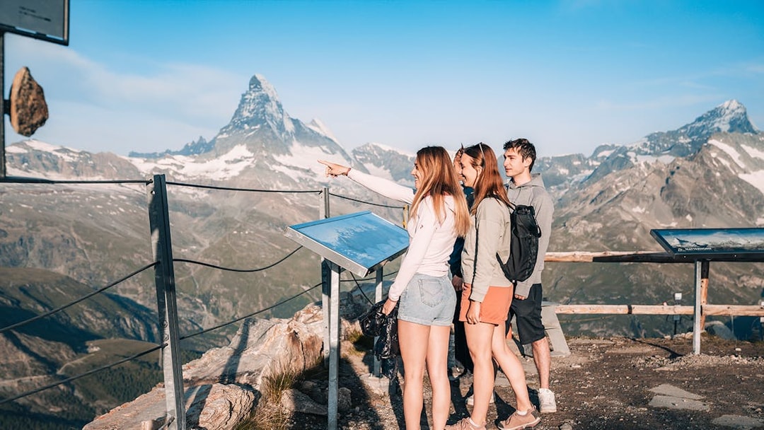 Tourists viewing Matterhorn from a glacier top with an information board in Zermatt, Switzerland.