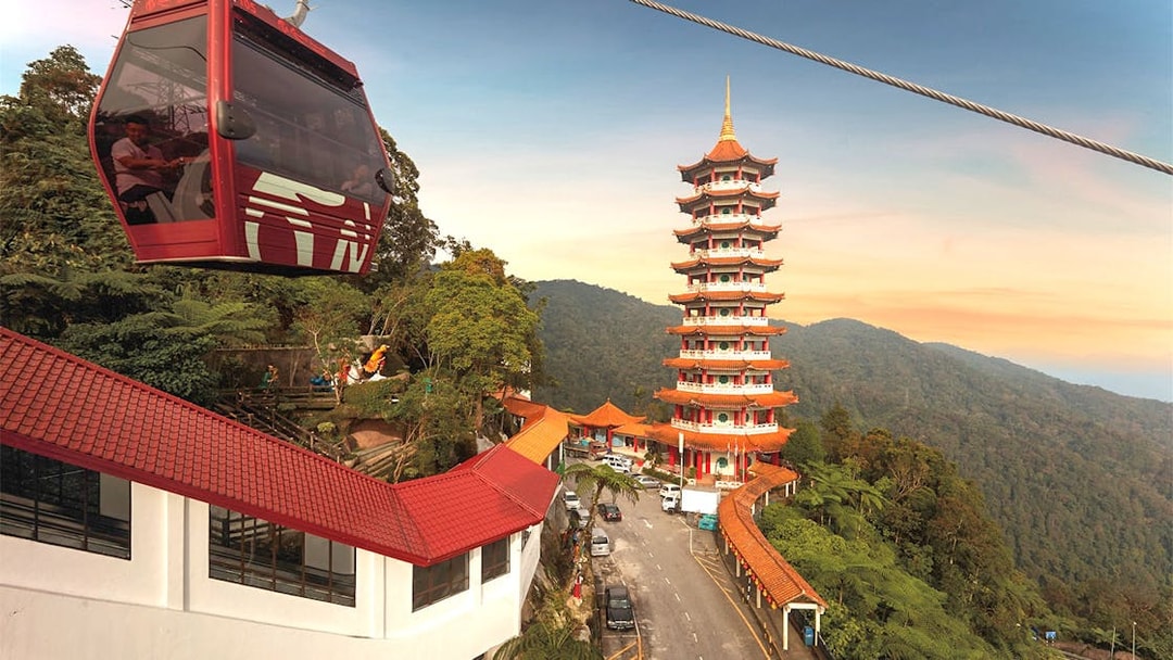 Genting Awana SkyWay cable car near pagoda tower in lush mountain landscape.