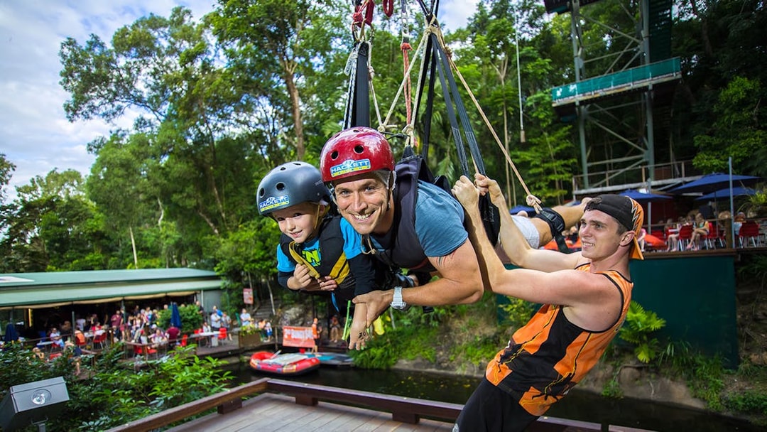 Participants on the Cairns Giant Swing, suspended in harnesses, surrounded by lush greenery.