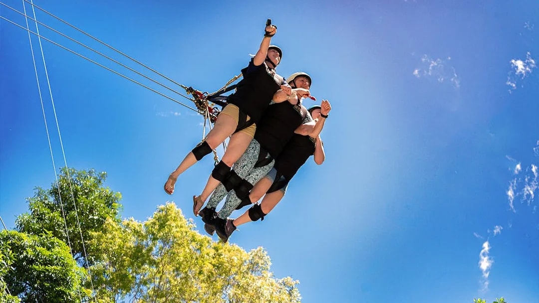 Three people on the Cairns Giant Swing against a clear blue sky.