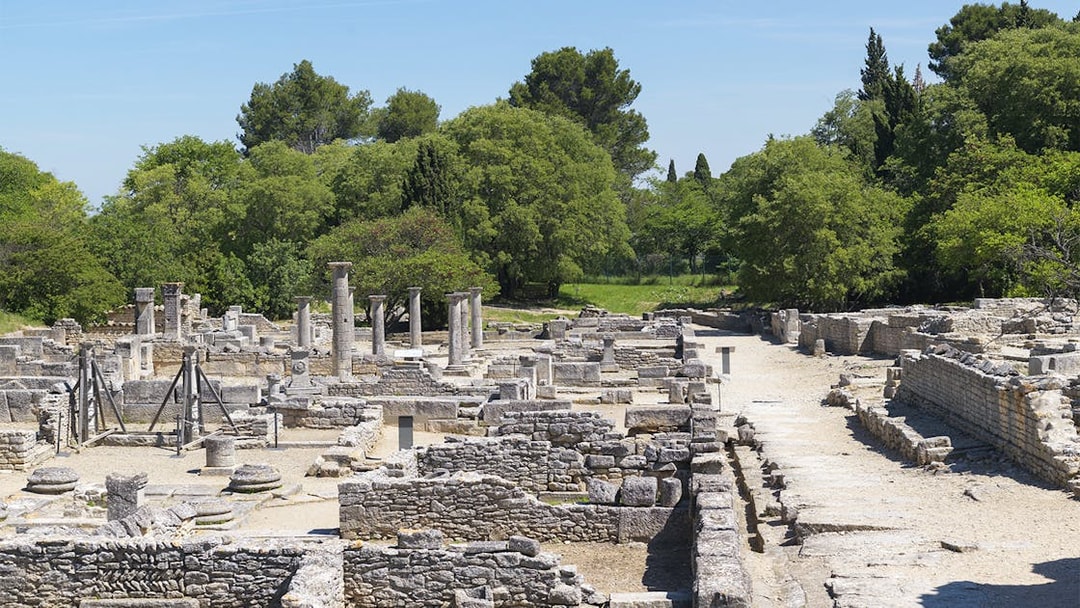 Glanum Archaeological Site ruins with stone columns and ancient structures in a green landscape.