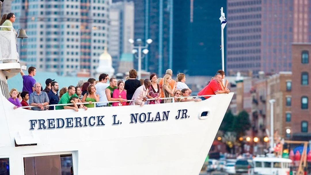 People on a cruise ship in Boston, enjoying city skyline views.