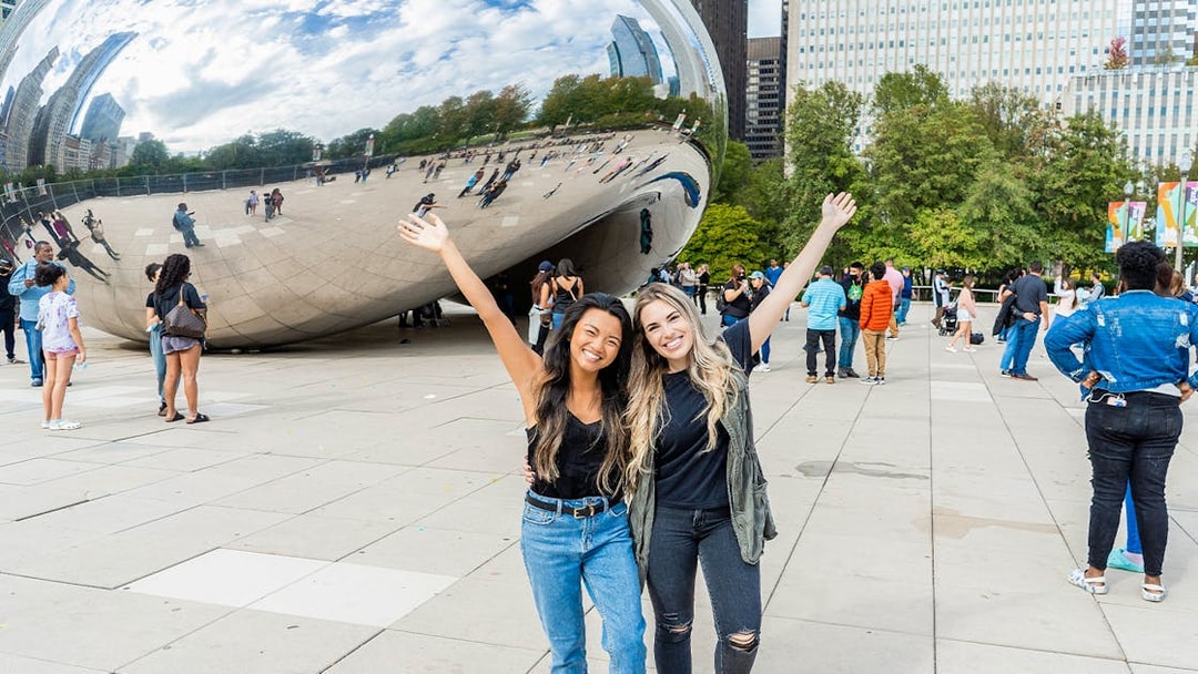 Tourists smiling in front of Cloud Gate sculpture in Chicago.