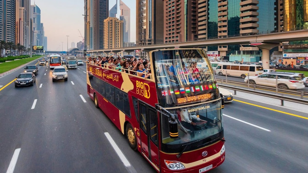 Open-top tour bus on Dubai highway with city skyscrapers in the background.