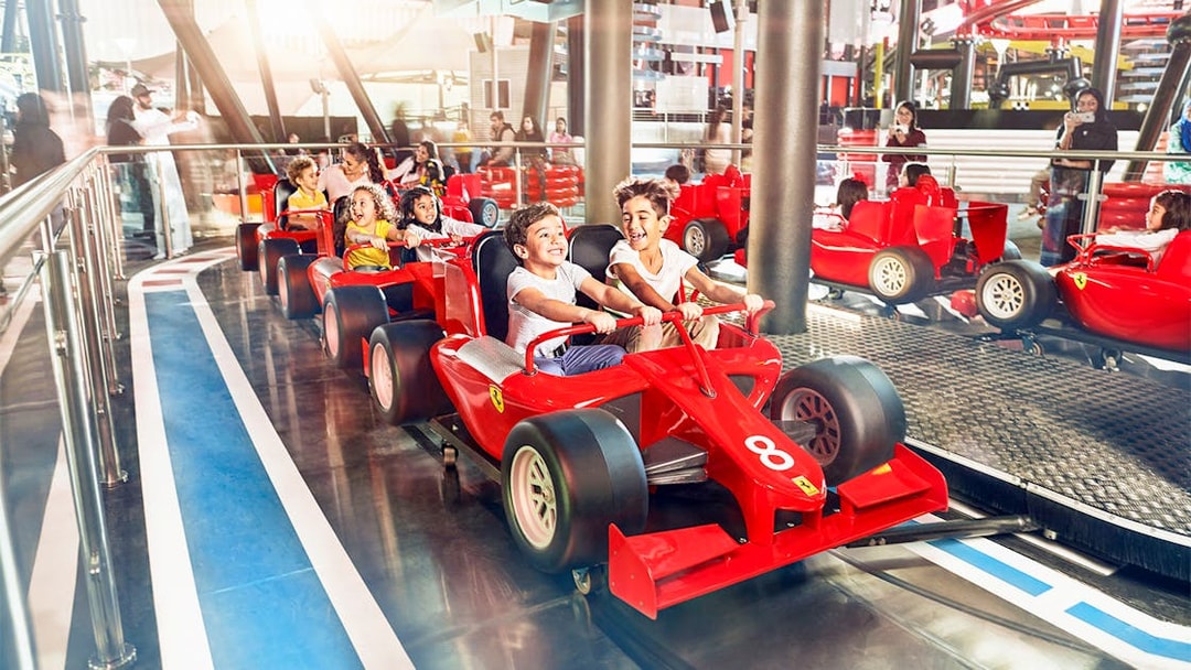 Children enjoying a ride in red race cars at a YAS Island theme park, Abu Dhabi.