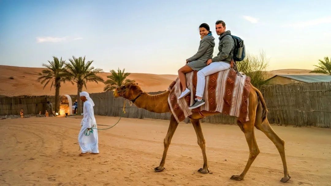 Couple on camel during Dubai desert safari with guide leading.