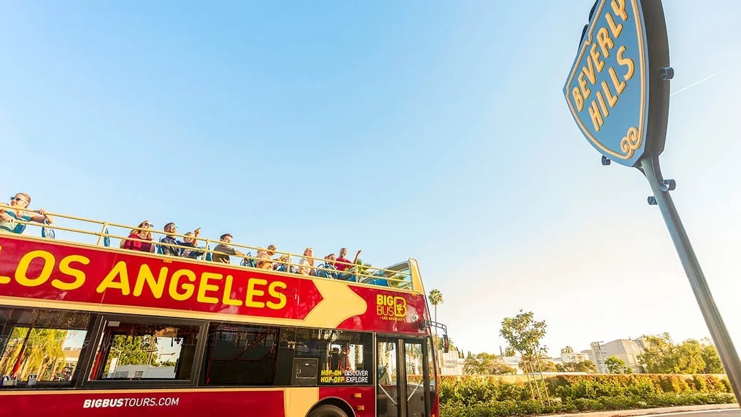 Open-top tour bus in Los Angeles near Beverly Hills sign.