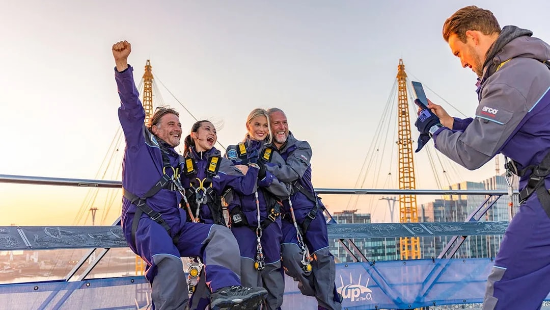 Climbers celebrating atop the O2 Arena roof with London's skyline in view.