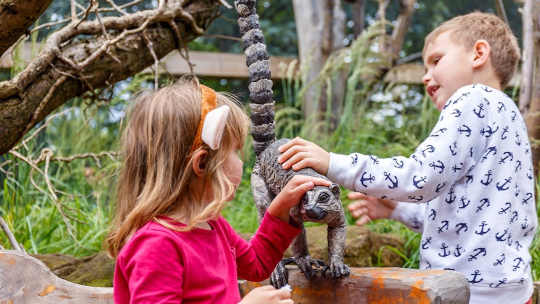 Children interacting with a lemur statue at a zoo.