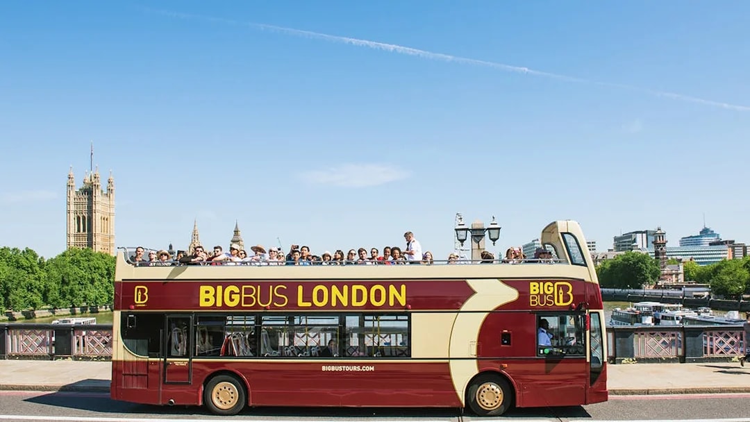 Open-top bus tour in London with tourists, passing by the Houses of Parliament.