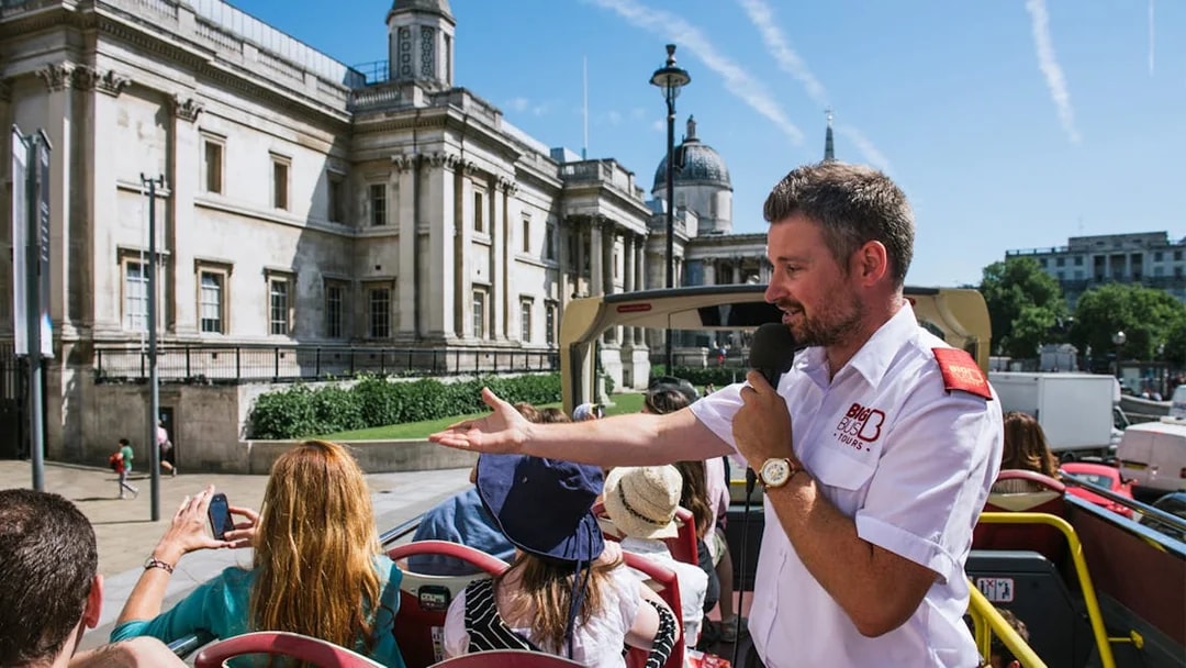 Tour guide speaking to tourists on an open-top bus near the National Gallery, London.