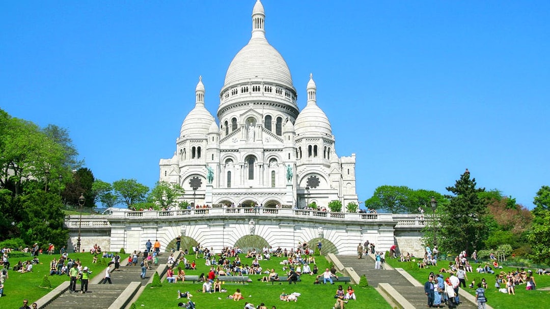 Sacré-Cœur Basilica in Montmartre, Paris with visitors on the steps and lawn.