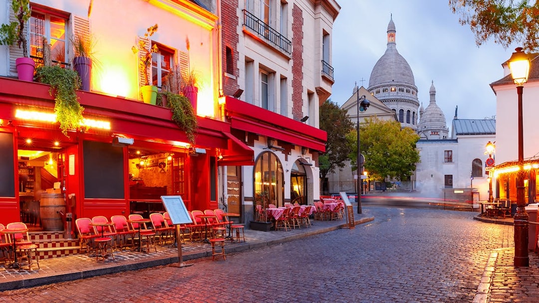 Montmartre street with Sacré-Cœur Basilica in Paris, featuring outdoor café seating.