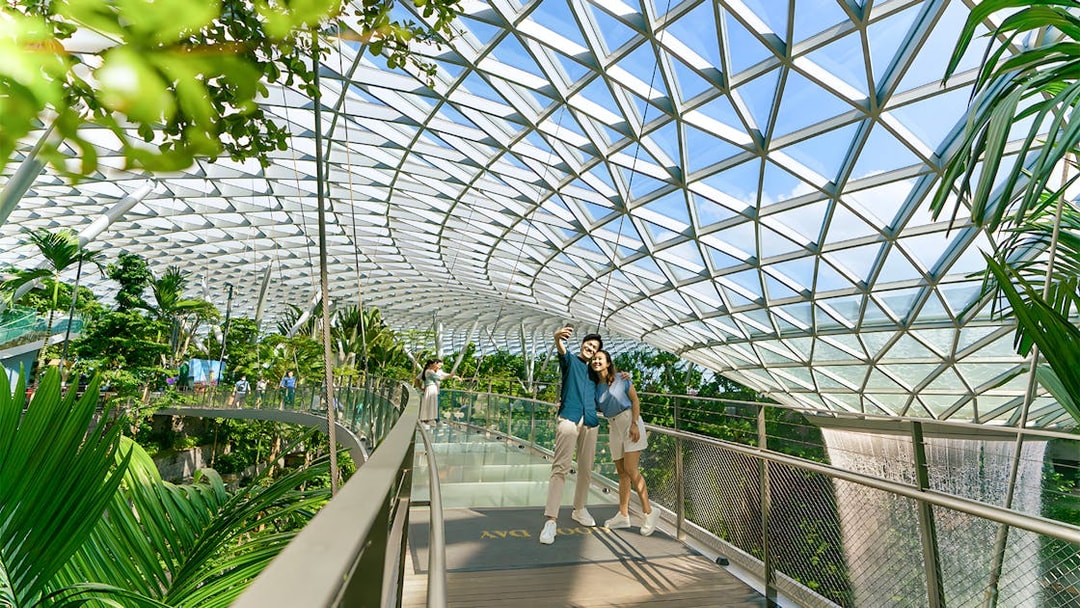 Couple taking selfie on walkway at Jewel Changi Airport, Singapore, under glass dome.