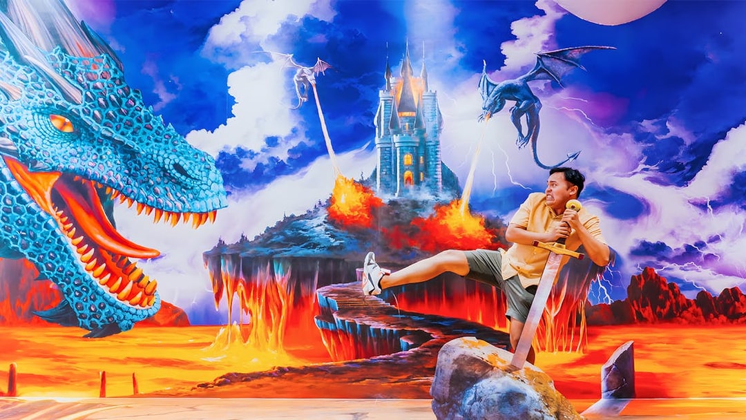 Man posing with sword in fantasy dragon mural at Trick Eye Museum, Singapore.