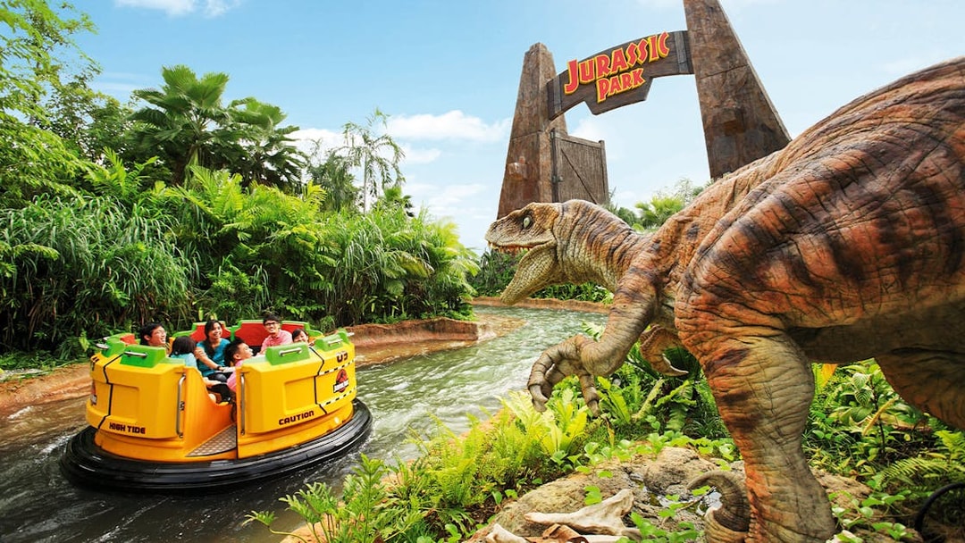 Visitors on Jurassic Park Rapids Adventure ride at Universal Studios Singapore, with dinosaur and jungle scenery.
