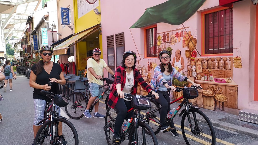 Cyclists exploring a vibrant street in Singapore with colorful murals and local shops.