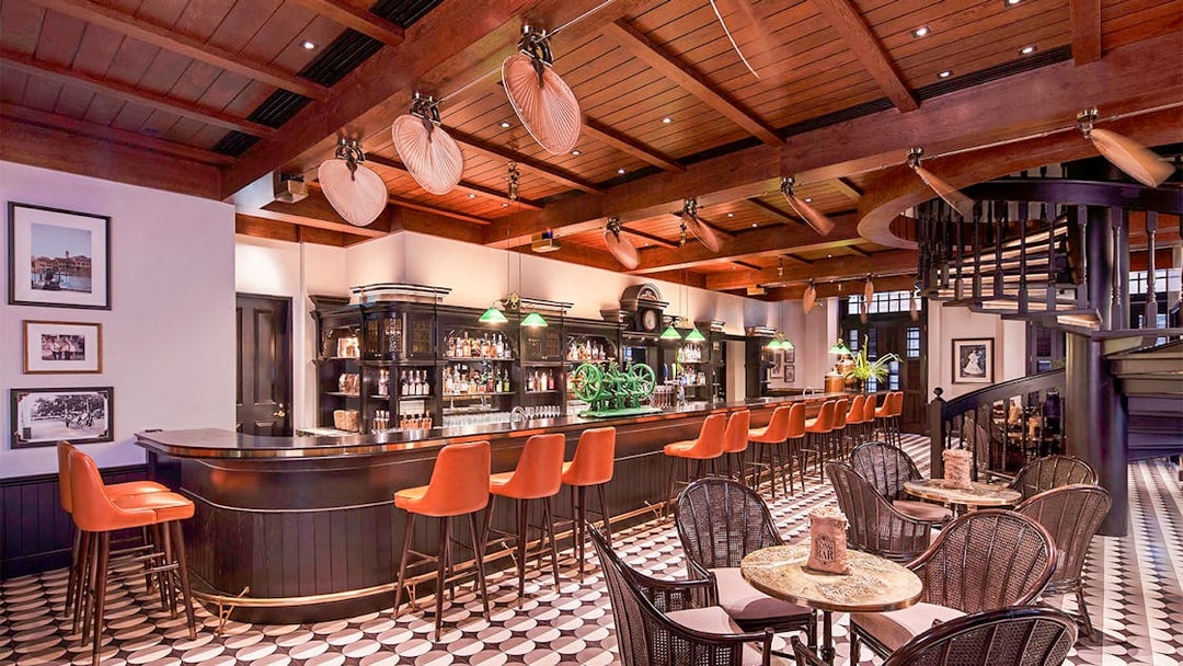 Bar interior with wooden ceiling, spiral staircase, and orange bar stools in Singapore.
