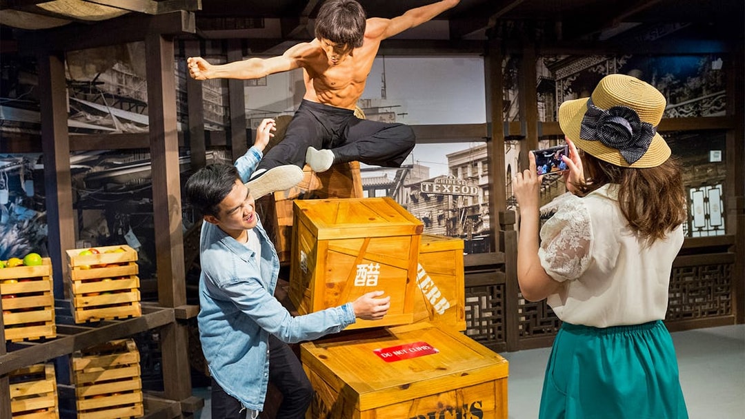 Man posing with Bruce Lee statue at Madame Tussauds Singapore, part of Go City Singapore Pass.