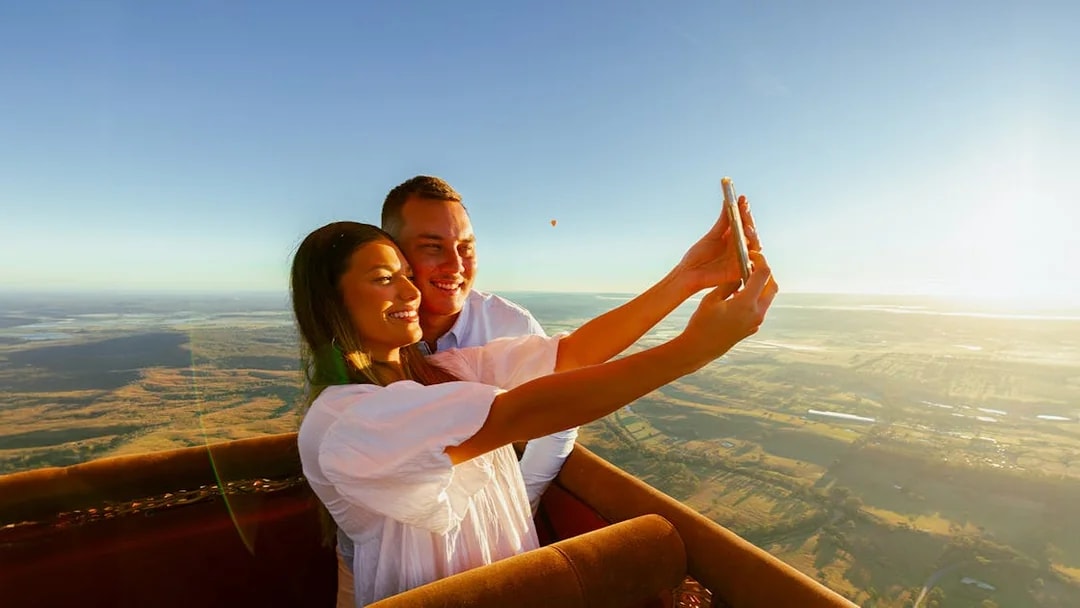 Couple taking a selfie in a hot air balloon over Gold Coast at sunrise.