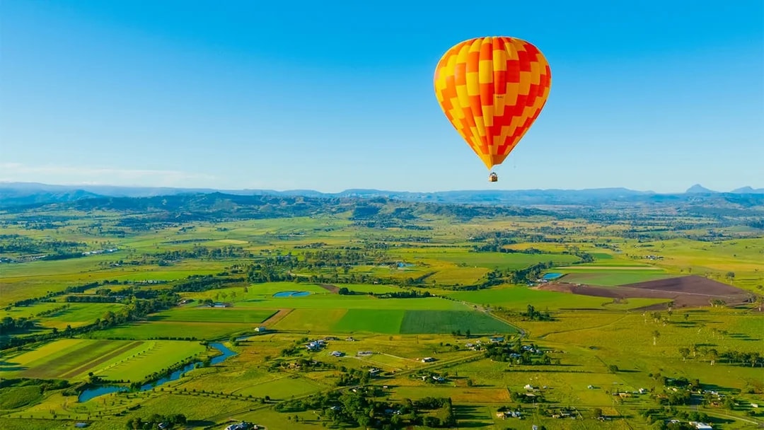 Hot air balloon over Gold Coast countryside, Australia, with fields and distant mountains.