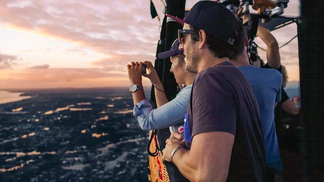 People enjoying a hot air balloon flight at sunset, capturing views over a scenic landscape.