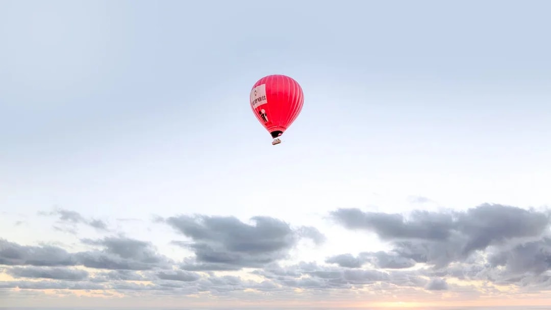 Hot air balloon floating over a cloudy sky at sunrise.