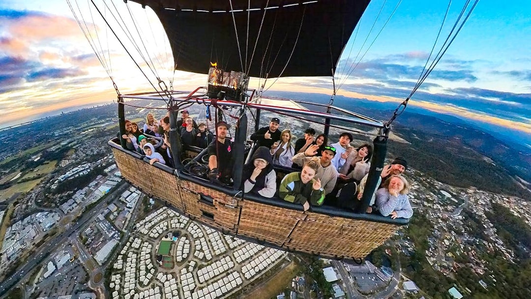 Group enjoying a hot air balloon flight over a cityscape at sunrise.