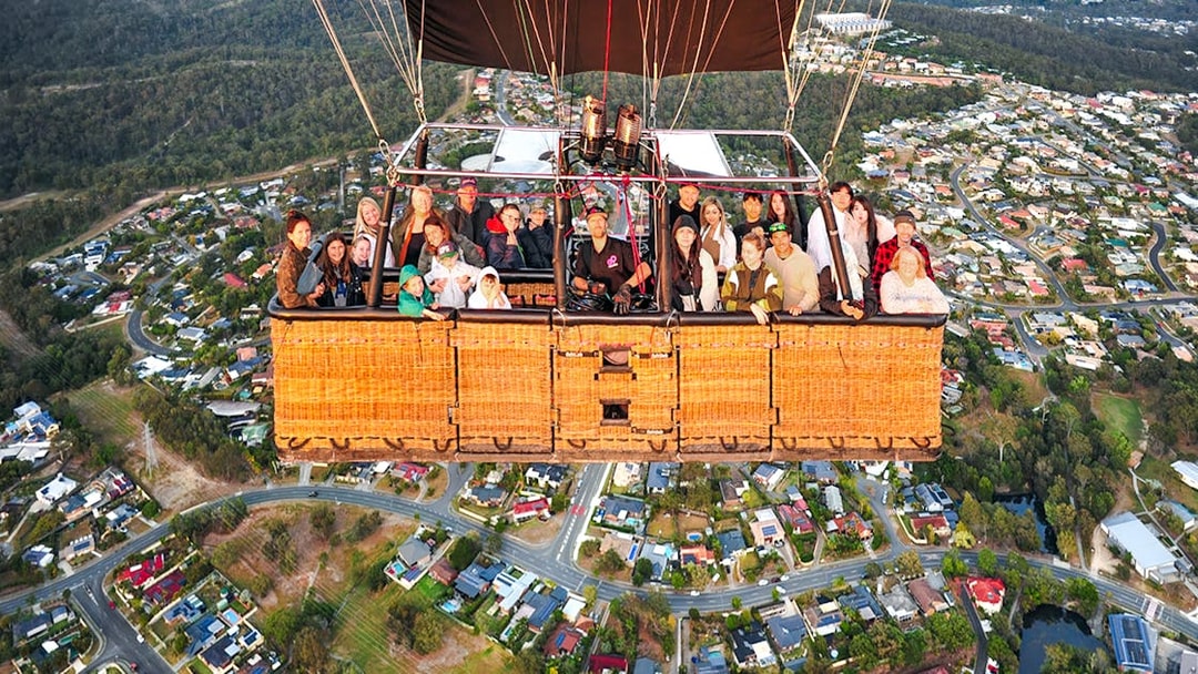 Group enjoying hot air balloon flight over suburban landscape.