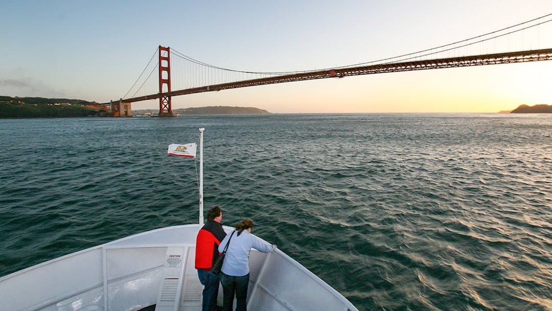 Couple on Golden Gate Bay cruise deck at sunset, viewing Golden Gate Bridge, San Francisco.