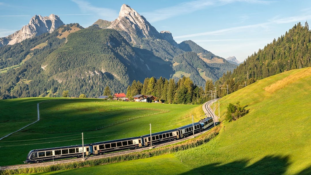 GoldenPass Express train traveling through lush green hills with Interlaken mountains in the background.