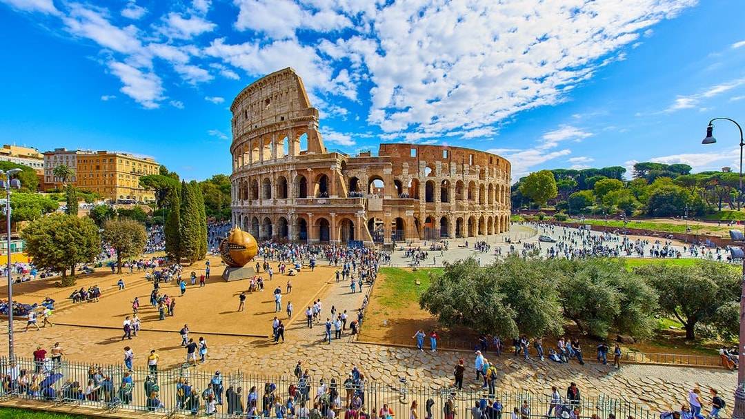 Colosseum in Rome with tourists exploring the area, viewed from a distance.