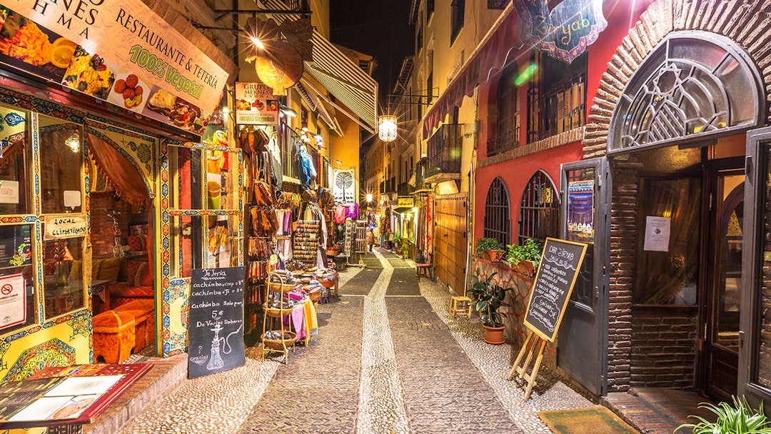 Narrow street in Granada with colorful shops and restaurants, part of the Alhambra and Cathedral tour.